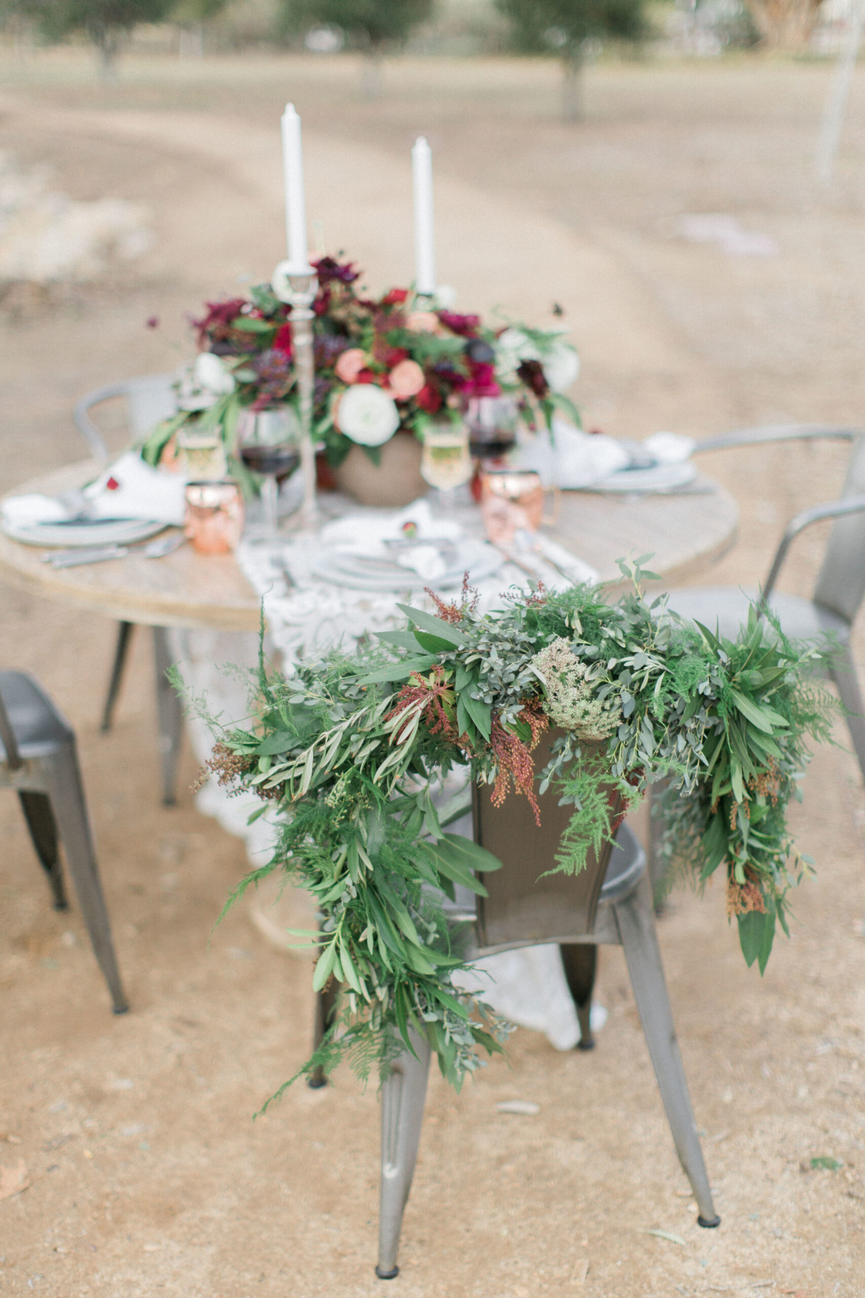 Greenery-decorated chair at a rustic outdoor wedding table.